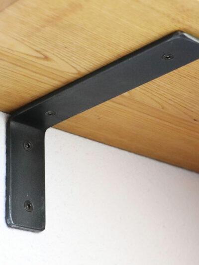 Équerre murale noire en acier patiné fixée sur un mur blanc