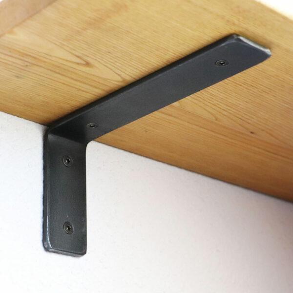 Équerre murale noire en acier patiné fixée sur un mur blanc